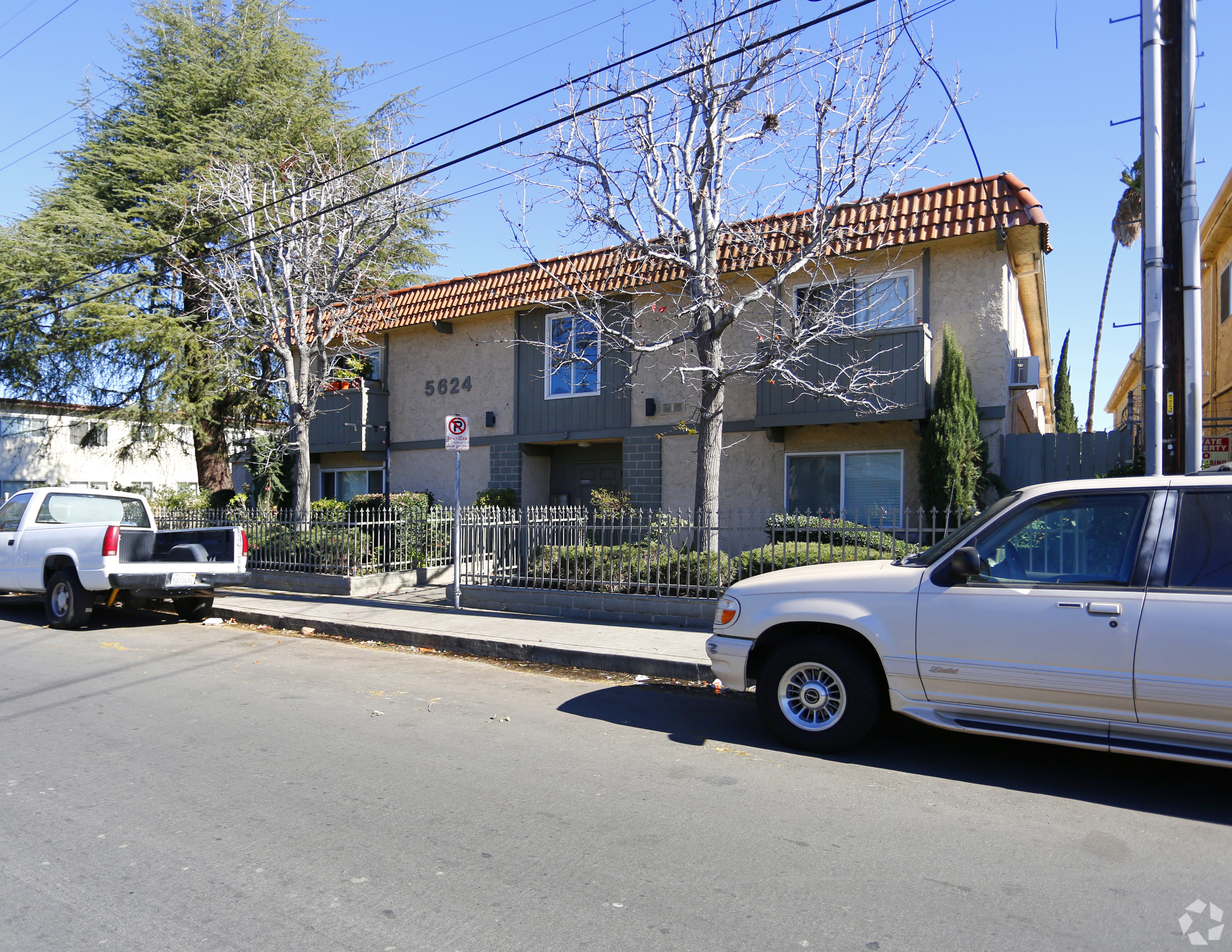 A white car is parked on the side of a street in front of a house with the number 5624 on it.